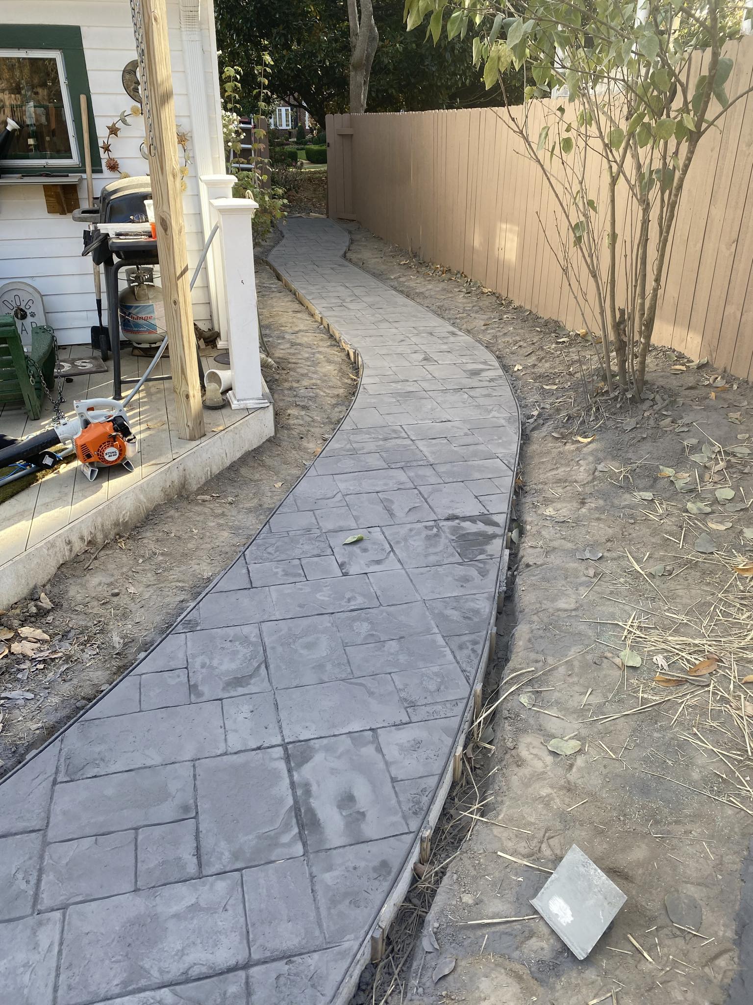 Curved stamped concrete walkway along a backyard fence